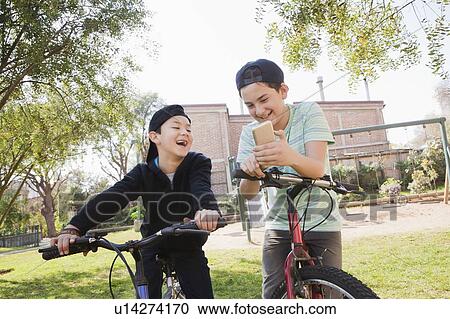 Boys looking at smart phone on their bicycles View Large Photo Image Stock Image - Boys looking at smart phone on their bicycles. Fotosearch