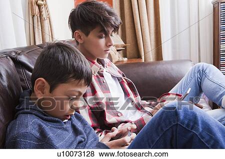 Stock Photo - Brothers using smart phones on sofa. Fotosearch
