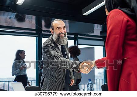 Stock Photo - Business partners shaking hands at meeting in office. Fotosearch