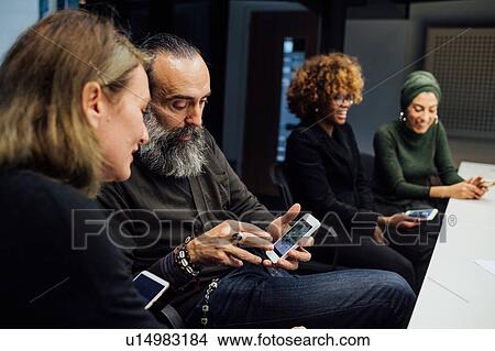 Business partners using smartphone at meeting in office View Large Photo Image Picture - Business partners using smartphone at meeting in office. Fotosearch