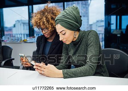 Stock Photography - Business partners using smartphone at meeting in office. Fotosearch