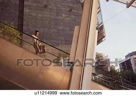 Stock Photo - Businessman descending escalator of office building, Milano, Lombardia, Italy. Fotosearch