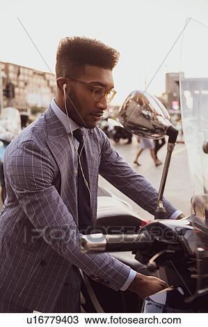 Stock Image - Businessman starting motorcycle on pavement. Fotosearch