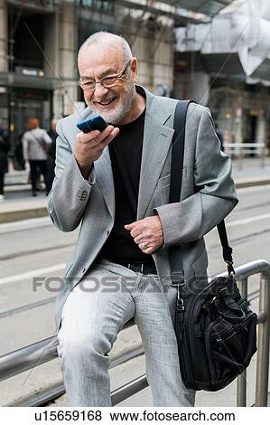 Stock Photo - Businessman talking into smartphone on pavement, Milan, Lombardia, Italy. Fotosearch