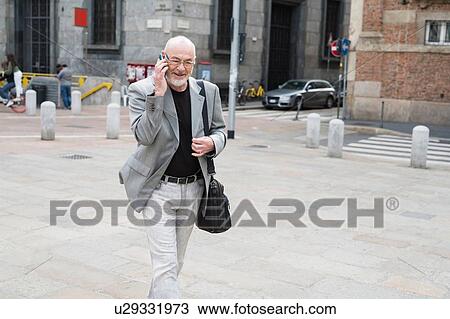 Stock Image - Businessman talking on smartphone in square, Milan, Lombardia, Italy. Fotosearch