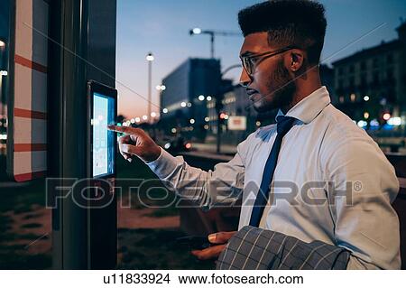 Picture - Businessman using digital information system at bus stop, Milano, Lombardia, Italy. Fotosearch