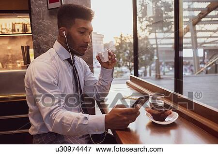 Stock Photo - Businessman using smartphone at tea time in cafe. Fotosearch