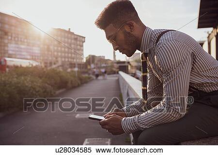 Stock Photography - Businessman using smartphone by pavement, Milano, Lombardia, Italy. Fotosearch