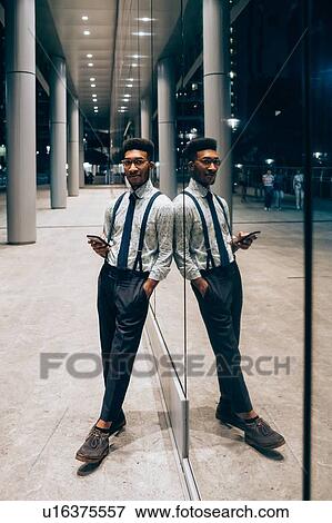 Businessman using smartphone, leaning against mirrored wall of office building, Milano, Lombardia, Italy View Large Photo Image Stock Photo - Businessman using smartphone, leaning against mirrored wall of office building, Milano, Lombardia, Italy. Fotosearch
