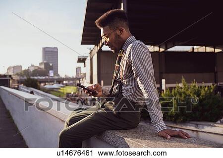 Stock Image - Businessman using smartphone on pavement, Milano, Lombardia, Italy. Fotosearch