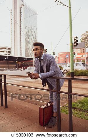 Stock Image - Businessman using smartphone on pavement, Milano, Lombardia, Italy. Fotosearch