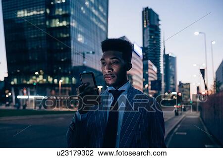Stock Image - Businessman using smartphone on pavement, Milano, Lombardia, Italy. Fotosearch