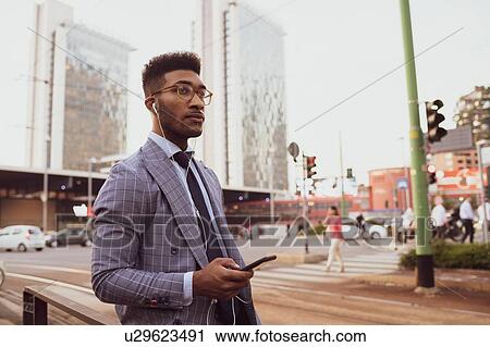 Stock Image - Businessman using smartphone on pavement, Milano, Lombardia, Italy. Fotosearch