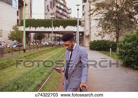 Stock Image - Businessman using smartphone on pavement, Milano, Lombardia, Italy. Fotosearch