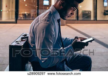 Stock Photo - Businessman using smartphone on pavement, Milano, Lombardia, Italy. Fotosearch