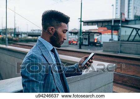 Stock Photo - Businessman using smartphone on pavement, Milano, Lombardia, Italy. Fotosearch