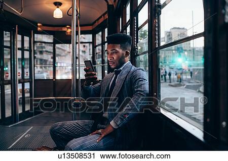 Stock Image - Businessman using smartphone on tram in city. Fotosearch