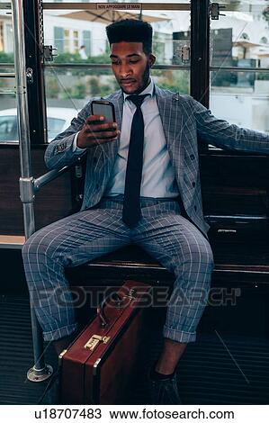 Stock Image - Businessman using smartphone on tram in city. Fotosearch