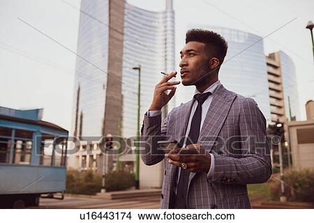Picture - Businessman using smartphone, smoking on pavement, Milano, Lombardia, Italy. Fotosearch