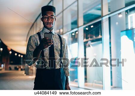Stock Photo - Businessman using smartphone, walking past shopfront, Milano, Lombardia, Italy. Fotosearch