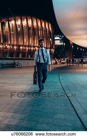 Stock Photograph - Businessman walking past buildings in city, Milano, Lombardia, Italy. Fotosearch