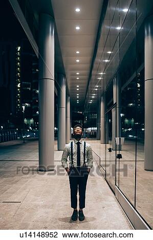 Stock Image - Businessman walking past mirrored wall of office building, Milano, Lombardia, Italy. Fotosearch
