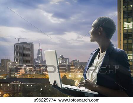 Businesswoman holding laptop by city skyline at sunset in Nairobi, Kenya View Large Photo Image Picture - Businesswoman holding laptop by city skyline at sunset in Nairobi, Kenya. Fotosearch