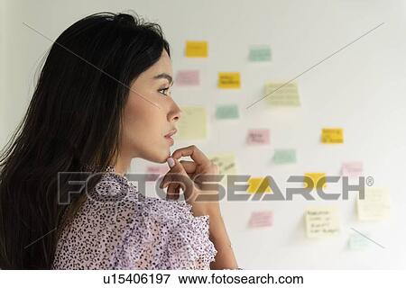 Stock Photo - Businesswoman thinking by wall of adhesive notes. Fotosearch