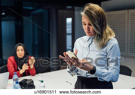 Stock Image - Businesswoman using smartphone at meeting in office. Fotosearch