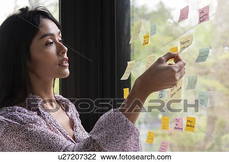 Stock Image - Businesswoman with adhesive notes on window. Fotosearch