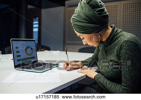 Businesswoman writing notes and using laptop in office View Large Photo Image Stock Photography - Businesswoman writing notes and using laptop in office. Fotosearch