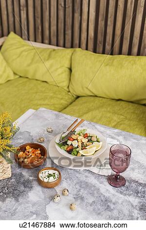 Picture - Caesar salad and sauce on table by sofa. Fotosearch