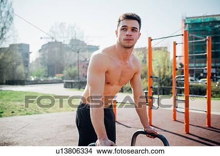 Picture - Calisthenics at outdoor gym, bare chested young man preparing to use exercise equipment. Fotosearch