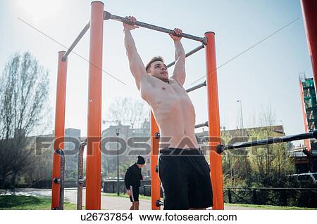 Calisthenics at outdoor gym, bare chested young man hanging from exercise equipment View Large Photo Image Picture - Calisthenics at outdoor gym, bare chested young man hanging from exercise equipment. Fotosearch