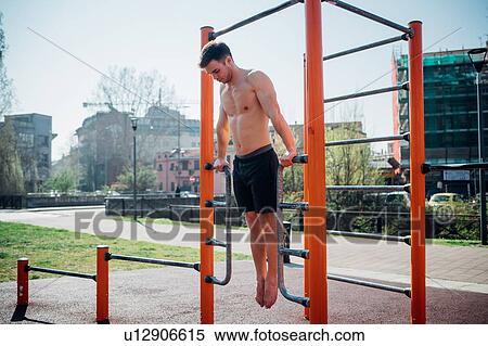 Stock Photography - Calisthenics at outdoor gym, bare chested young man doing backward push ups on exercise equipment. Fotosearch
