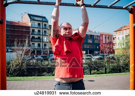 Stock Image - Calisthenics at outdoor gym, mature man doing pull up on exercise equipment. Fotosearch