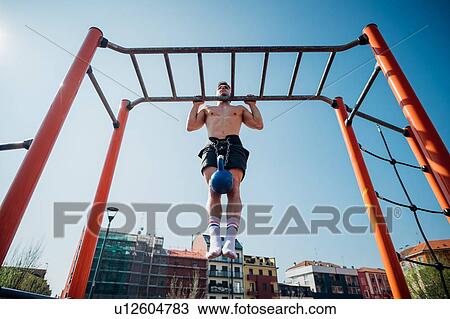 Calisthenics at outdoor gym, young man doing pull ups on exercise equipment with kettlebell on waist harness View Large Photo Image Stock Image - Calisthenics at outdoor gym, young man doing pull ups on exercise equipment with kettlebell on waist harness. Fotosearch