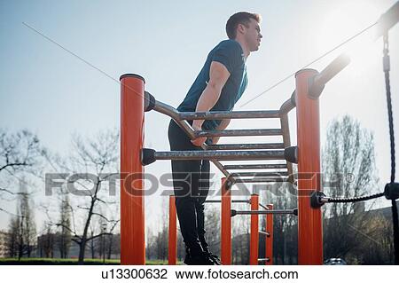 Stock Image - Calisthenics at outdoor gym, young man doing push ups on exercise equipment. Fotosearch