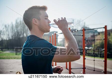 Stock Image - Calisthenics at outdoor gym, young man drinking bottled water. Fotosearch