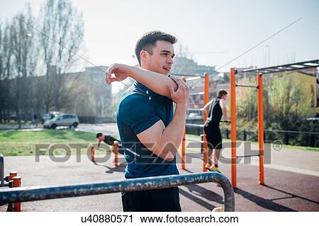 Stock Image - Calisthenics at outdoor gym, young man stretching arm. Fotosearch