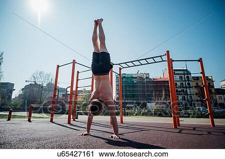 Stock Image - Calisthenics at outdoor gym, young man doing handstand, rear view. Fotosearch
