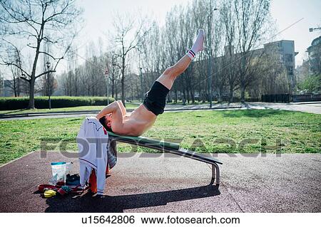 Stock Photograph - Calisthenics at outdoor gym, young man on weights bench with legs raised. Fotosearch