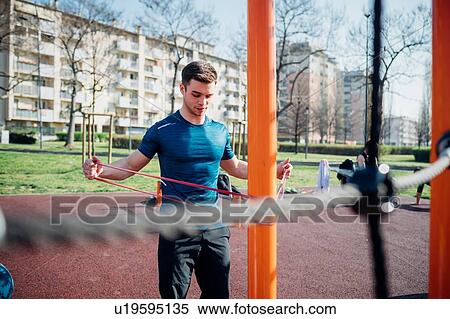 Stock Photography - Calisthenics at outdoor gym, young man stretching arms on exercise equipment. Fotosearch