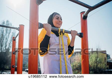 Stock Image - Calisthenics at outdoor gym, young woman doing pull up on exercise equipment. Fotosearch