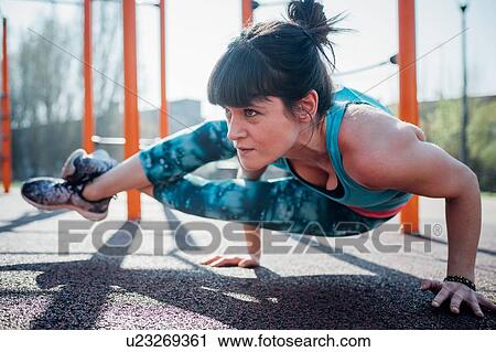 Stock Image - Calisthenics at outdoor gym, young woman with legs raised balancing on hands. Fotosearch