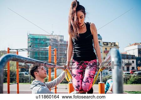 Picture - Calisthenics class at outdoor gym, male trainer encouraging young woman on parallel bars. Fotosearch