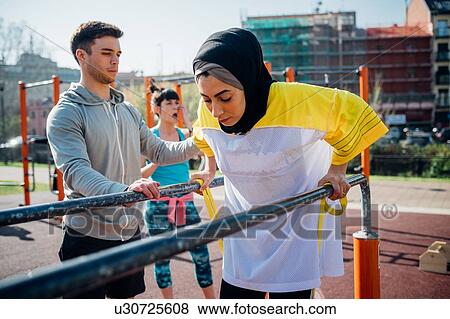 Calisthenics class at outdoor gym, male trainer encouraging young woman on parallel bars View Large Photo Image Stock Photo - Calisthenics class at outdoor gym, male trainer encouraging young woman on parallel bars. Fotosearch