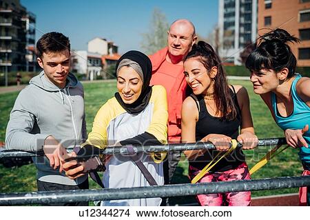 Picture - Calisthenics class at outdoor gym, men and women taking smartphone selfie. Fotosearch
