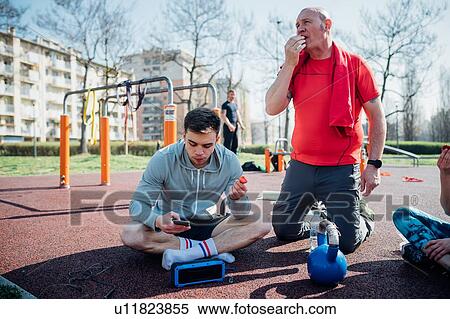 Calisthenics class at outdoor gym, men sitting looking at smartphone and eating fruit View Large Photo Image Stock Photography - Calisthenics class at outdoor gym, men sitting looking at smartphone and eating fruit. Fotosearch