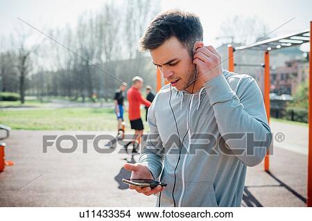 Calisthenics class at outdoor gym, young man putting in earphones View Large Photo Image Picture - Calisthenics class at outdoor gym, young man putting in earphones. Fotosearch